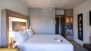 Een hotelkamer met een groot bed, nachtkastje, lamp en een klein zithoekje.
