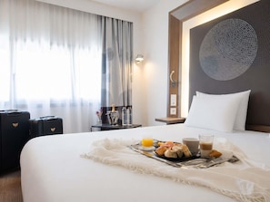 A hotel room with a bed, breakfast tray, and two black suitcases.