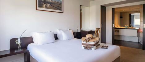 A hotel room with a large bed, a desk, a chair, a bathroom with a mirror, and a painting on the wall.
