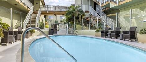 A swimming pool with a metal ladder, surrounded by wicker chairs and a palm tree.