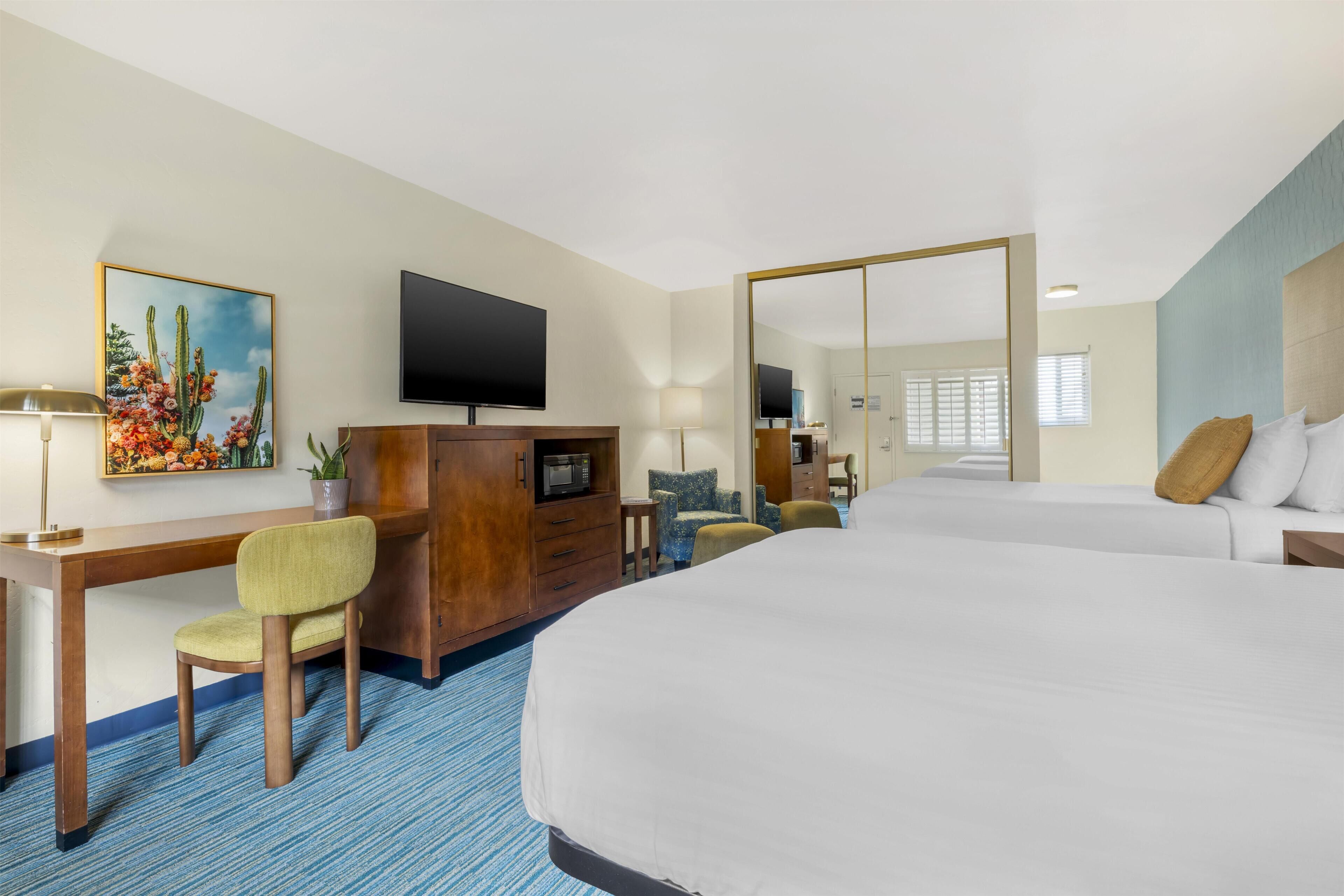 Ein Hotelzimmer mit einem großen Bett, einem Schreibtisch mit Stuhl, einem Fernseher, einem Spiegel und einem Fenster.
