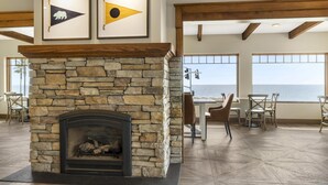 Una chimenea de piedra con obras de arte enmarcadas encima, un comedor con sillas y una mesa, y ventanas amplias con vistas.