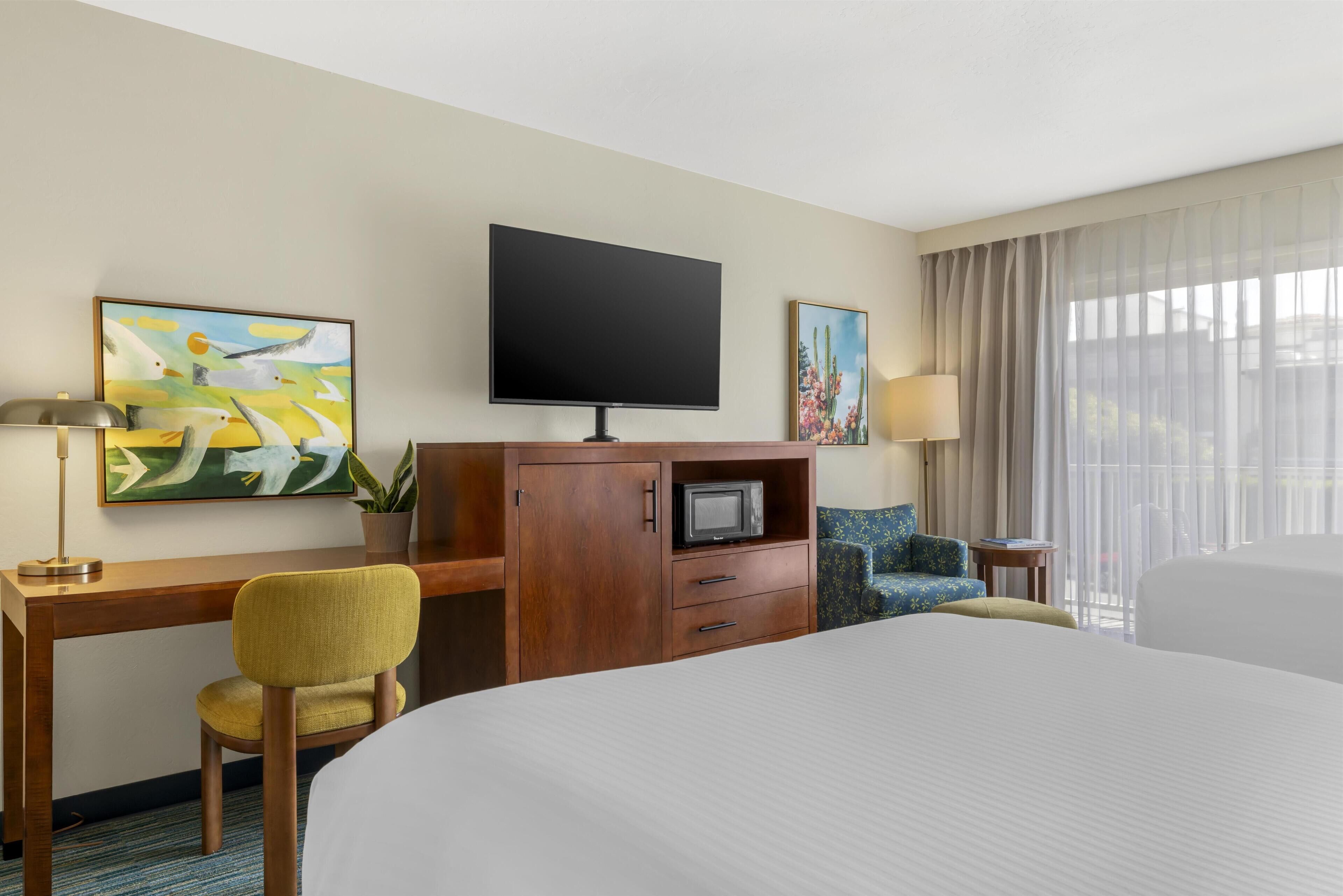 A hotel room with a large bed, a desk with a chair, a television, and artwork on the walls.
