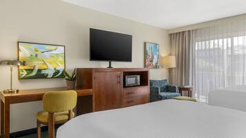 A hotel room with a large bed, a desk with a chair, a television, and artwork on the walls.