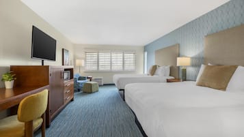 Une chambre d’hôtel équipée d’un bureau, de deux lits, d’une télévision et d’une fenêtre avec des stores.