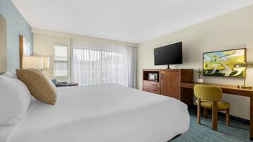 A hotel room with a bed, a desk, a chair, a television, and a painting on the wall.