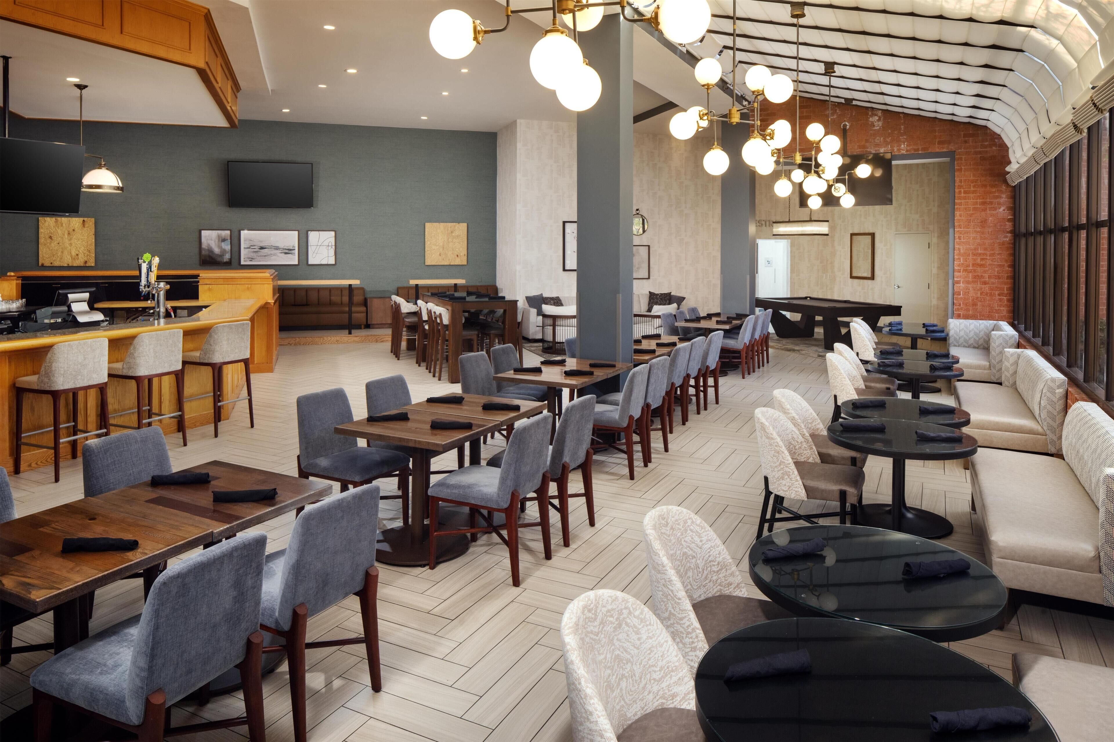 Un amplio comedor con varias mesas y sillas, una zona de bar y un área de estar con sofás y mesas redondas.