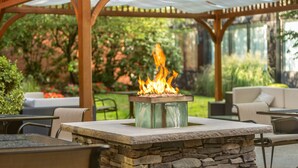 An outdoor patio with a stone fire pit and seating area under a wooden pergola.
