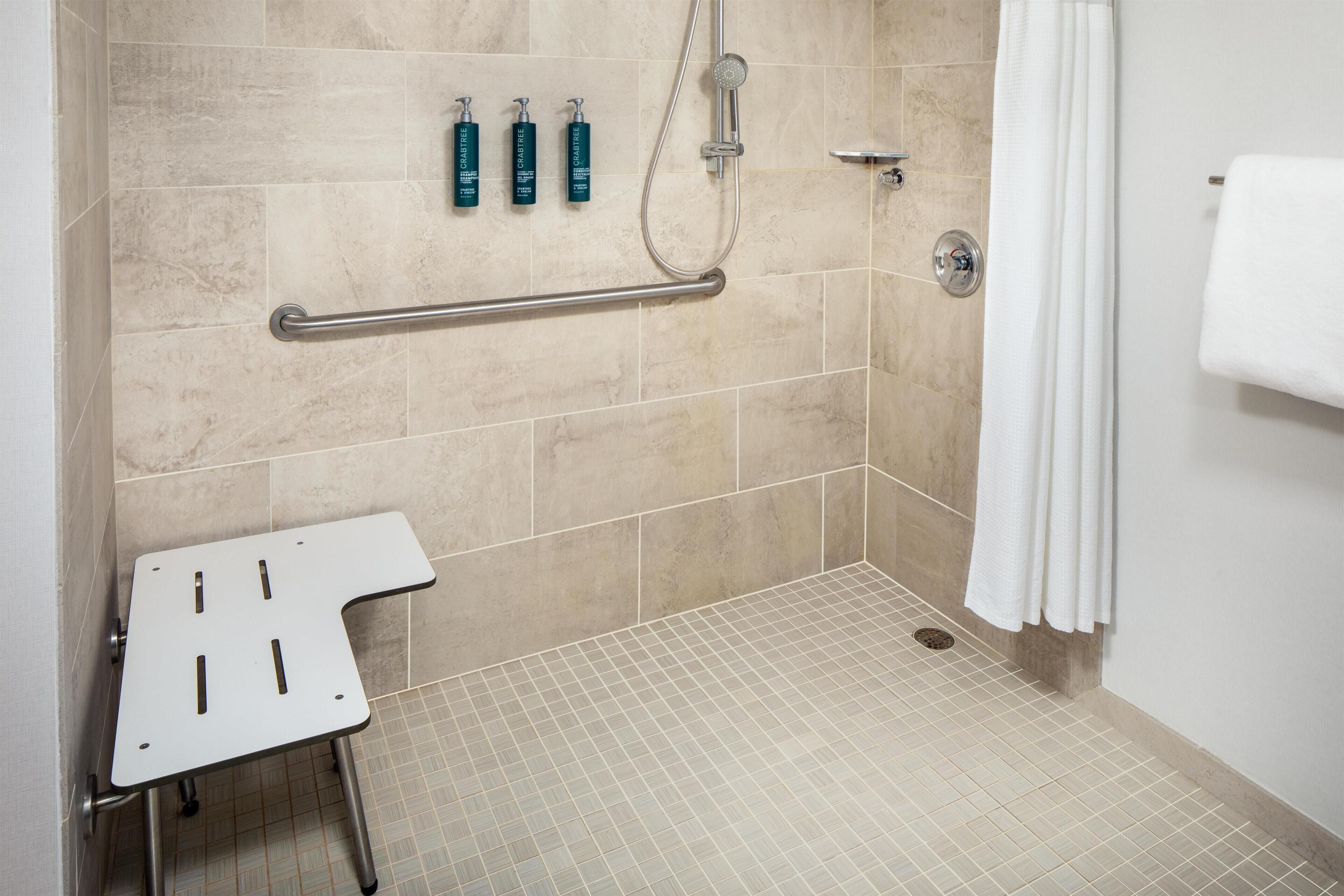 A bathroom with a shower, grab bar, and three bottles of shampoo.