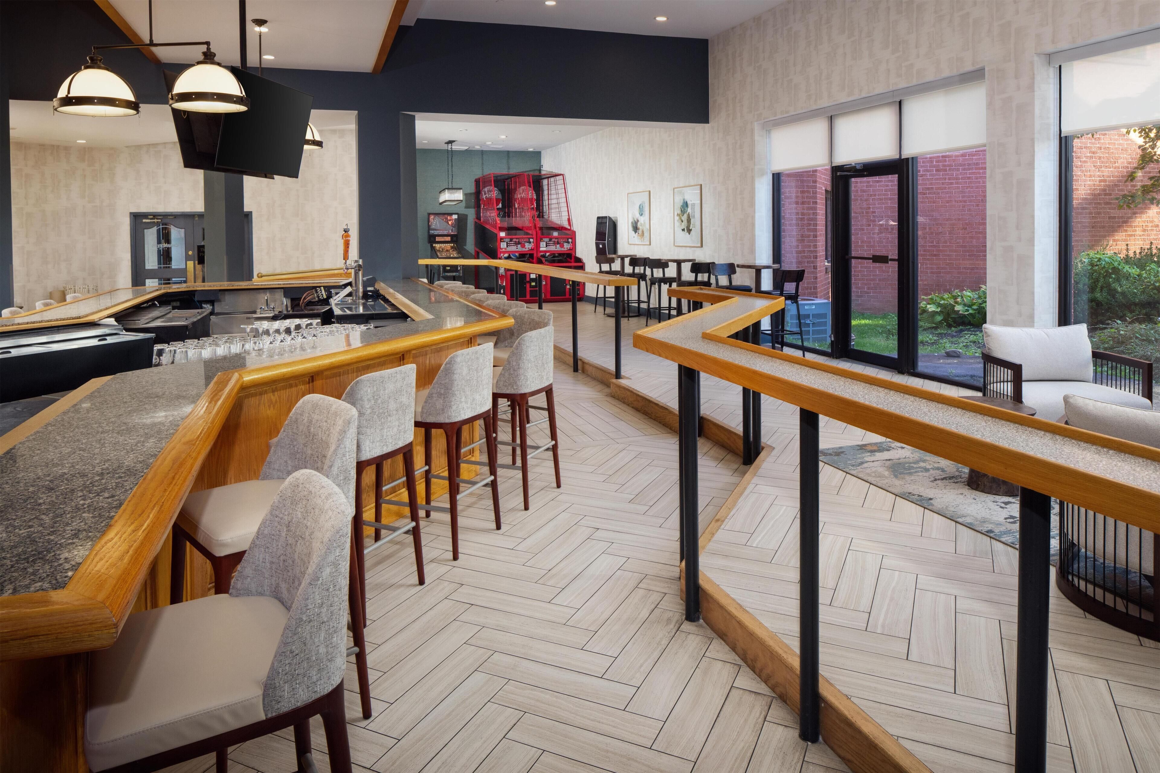 Een moderne bar met houten toogbladen, beklede barkrukken en hanglampen.