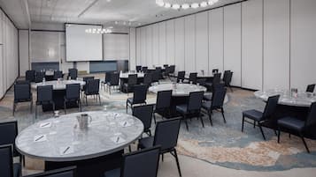 Un salón de conferencias con varias mesas redondas, sillas negras y una pantalla grande.