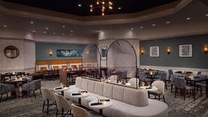 A spacious hotel lobby with a central seating area, multiple dining tables, and wall-mounted artwork.