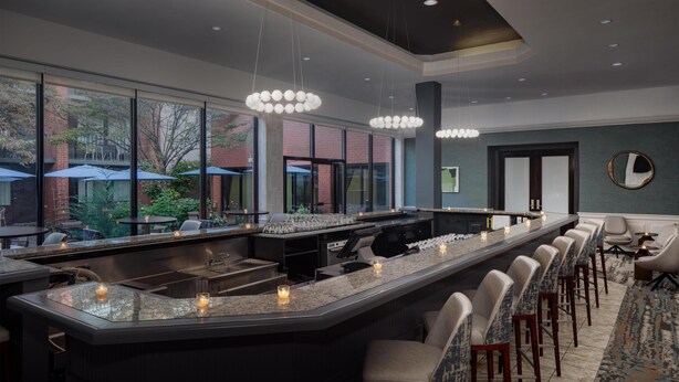 A modern bar area with a long counter, bar stools, and large windows overlooking a garden.