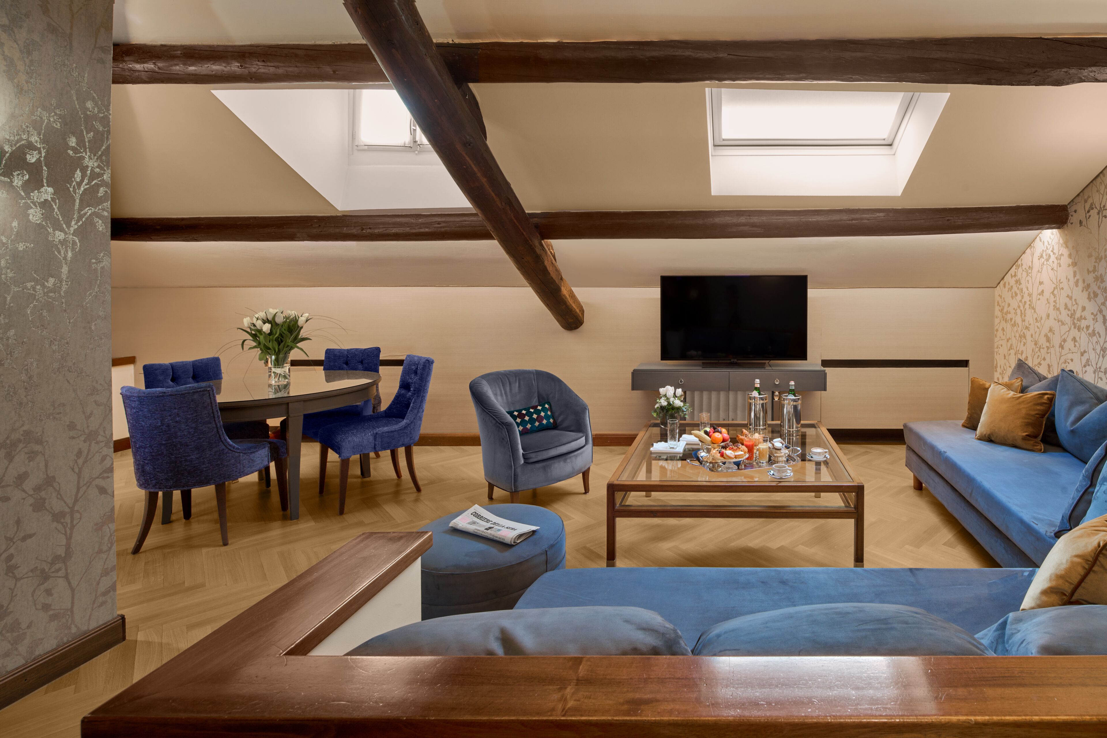 Una sala de estar con techo de madera, un comedor con sillas azules, un sofá y un televisor.
