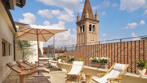 A rooftop terrace with lounge chairs, a large umbrella, and potted plants. A historic tower is visible in the background. - Hotel Accademia (Verona)