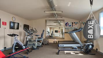 Ein Fitnessraum mit Trainingsgeräten, darunter ein Ergometer, ein Crosstrainer, ein Laufband und ein Sandsack.