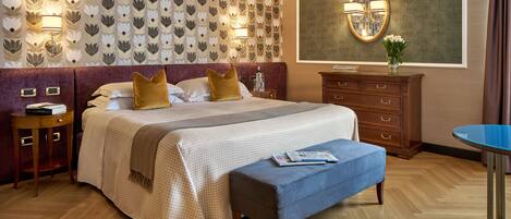 Habitación de hotel con una cama grande, una mesita de noche, un aparador, una mesa redonda y una pared con estampado floral.