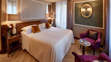 Una habitación de hotel con una cama grande, un área de descanso con una mesa y sillas, un espejo y una lámpara fijada a la pared.