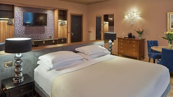Een hotelkamer met een groot bed, een flatscreen televisie aan de muur, een houten dressoir, een bureau met stoel en een kroonluchter.