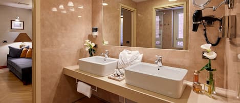 A hotel bathroom with two sinks, a large mirror, a hairdryer, and a towel rack.