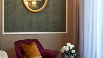 A room with a purple armchair, a small round table with a vase of flowers, and a wall-mounted light fixture.