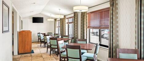 A hotel dining area with multiple tables and chairs, a wooden podium, and a television mounted on the wall.