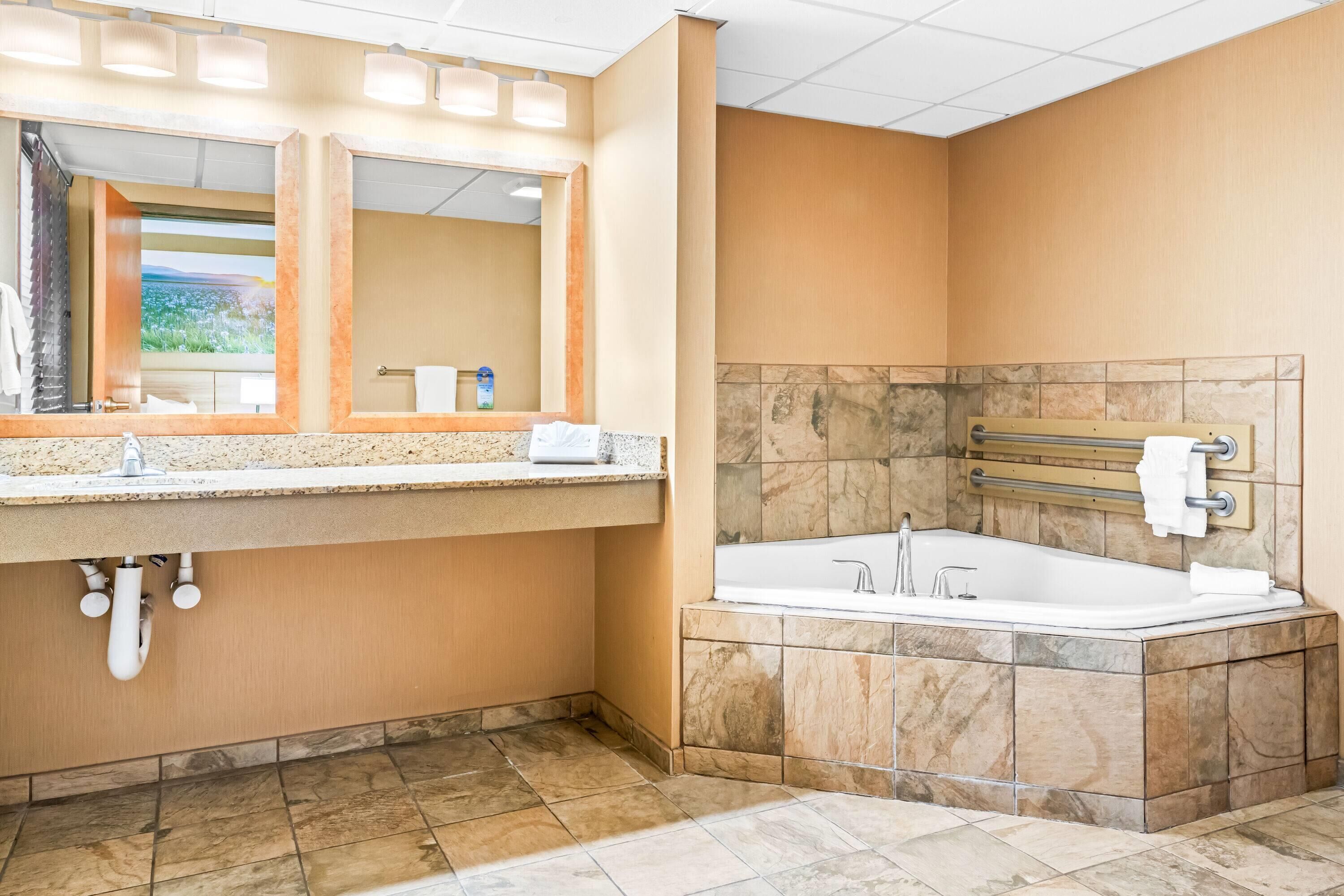 A modern bathroom with a large mirror, a bathtub, and a vanity with a sink.