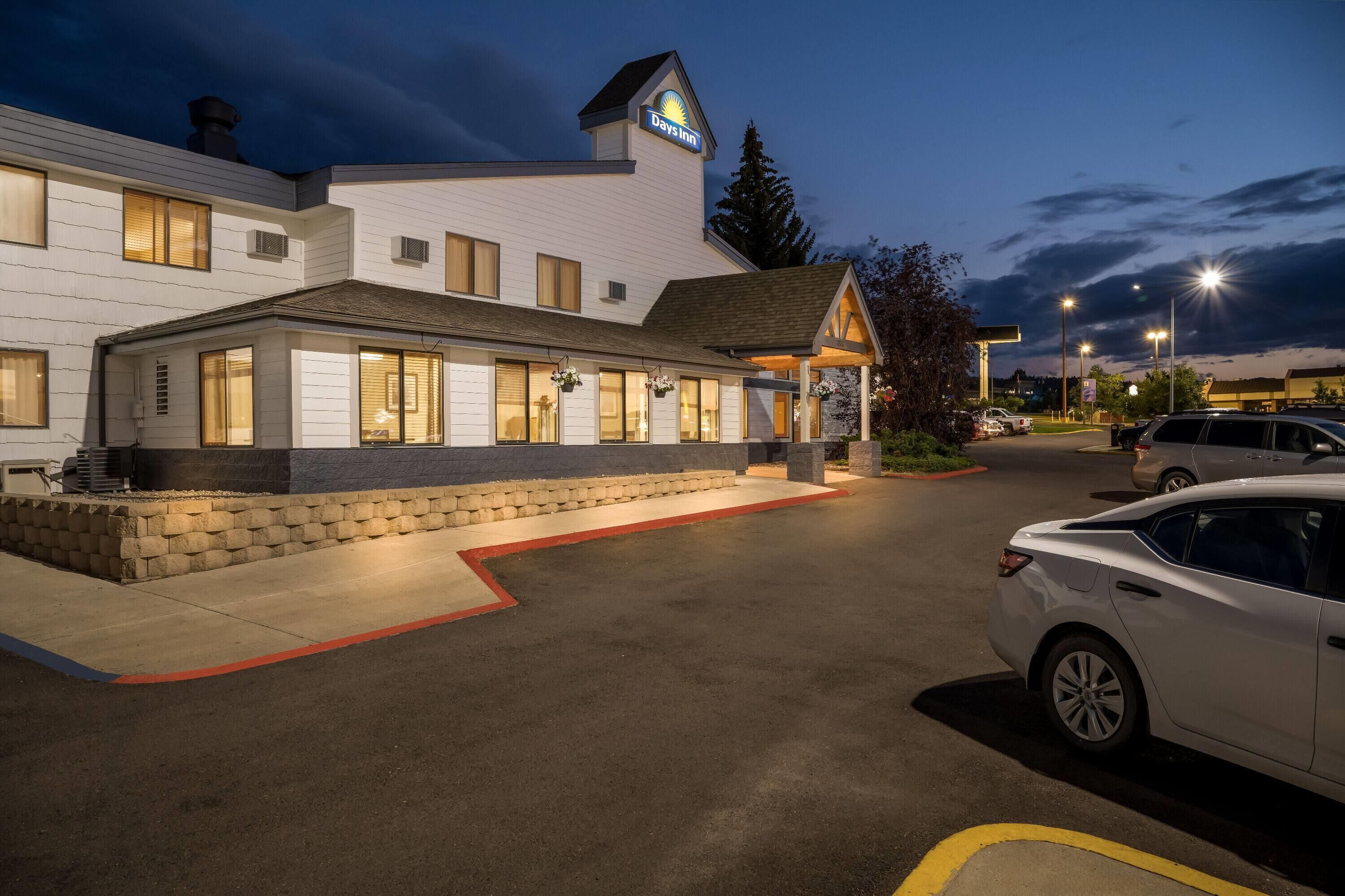 A Days Inn with a modern design, featuring a well-lit entrance and a parking area with several cars.