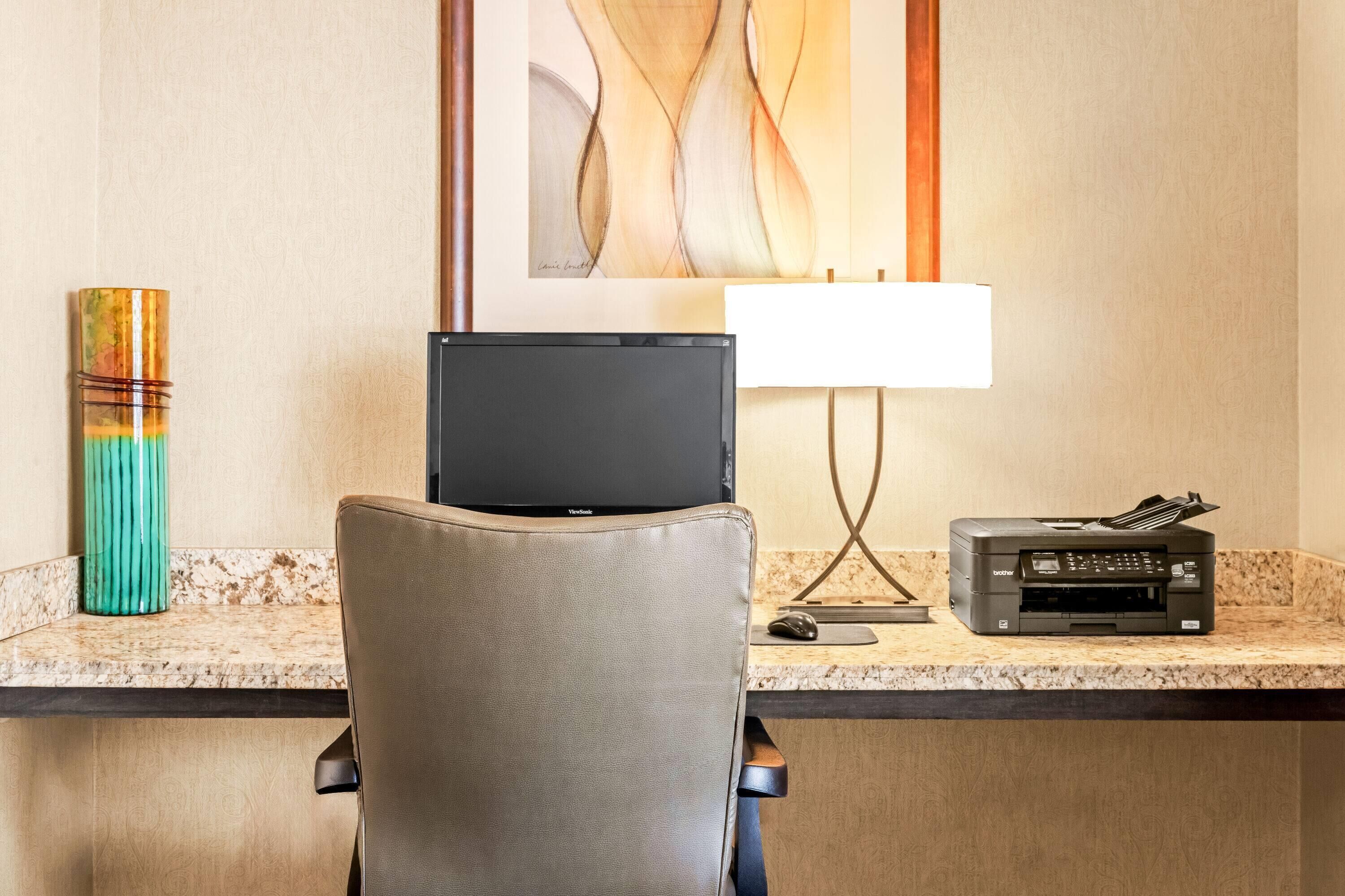 A hotel workspace with a laptop, printer, and a lamp on a marble countertop.