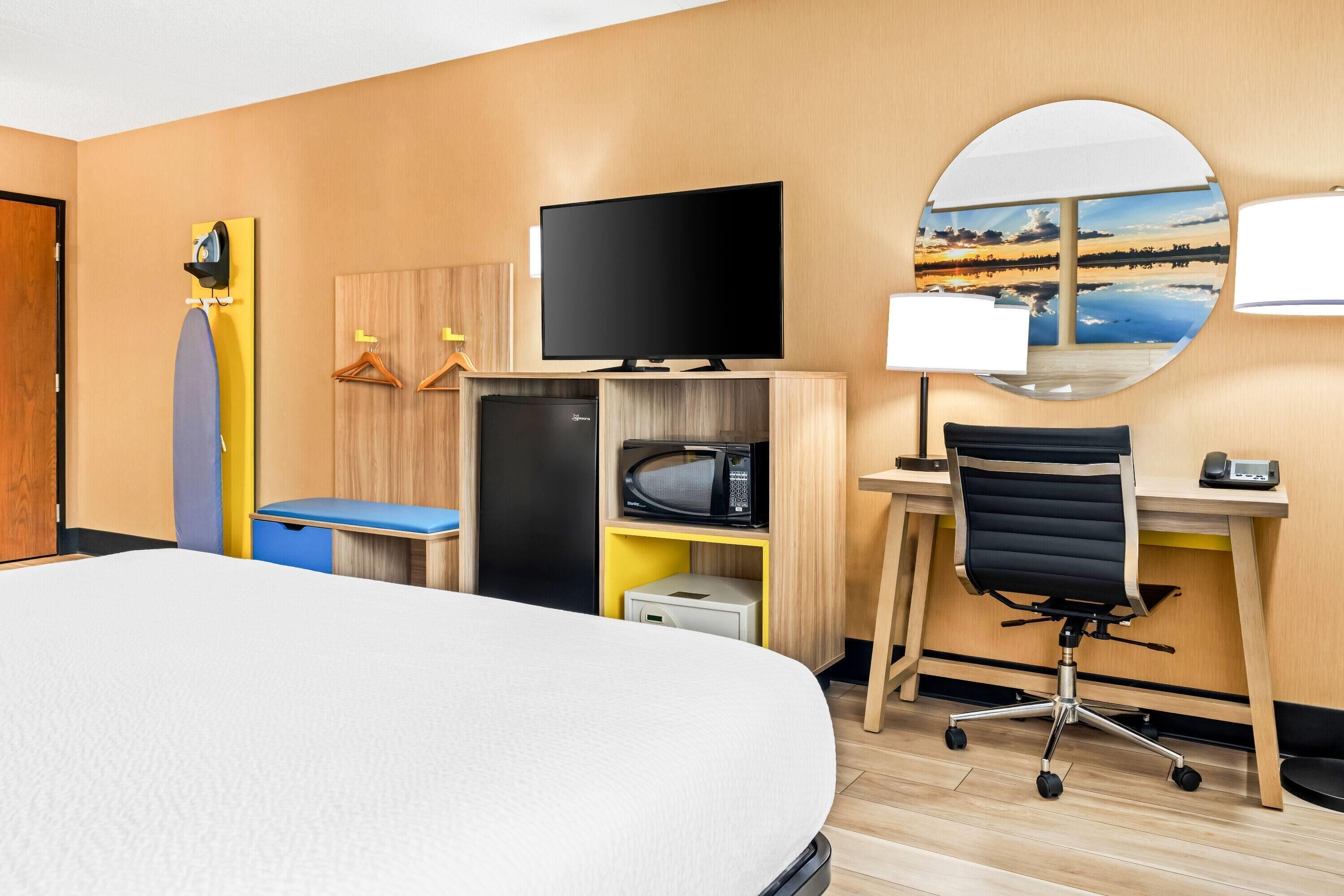 A hotel room with a bed, a desk with a computer, a TV, a microwave, and a small fridge.