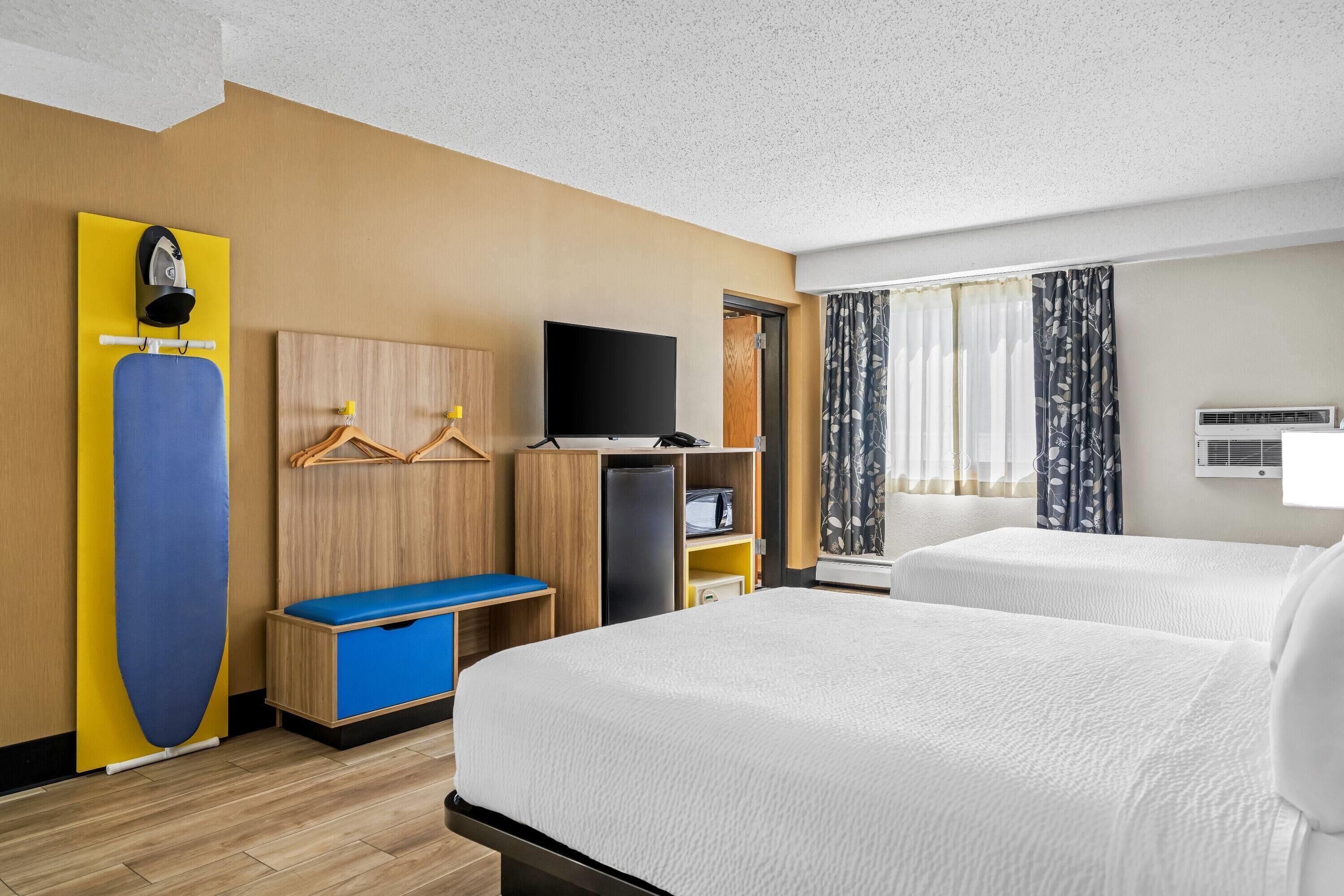A hotel room with two beds, a TV, a desk with a computer, a wardrobe, and a window with curtains.