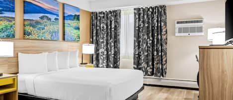 Ein Hotelzimmer mit einem großen Bett, einem Schreibtisch, einem Stuhl und einem Fernseher. An der Wand hängen drei Bilder und ein Klimagerät.