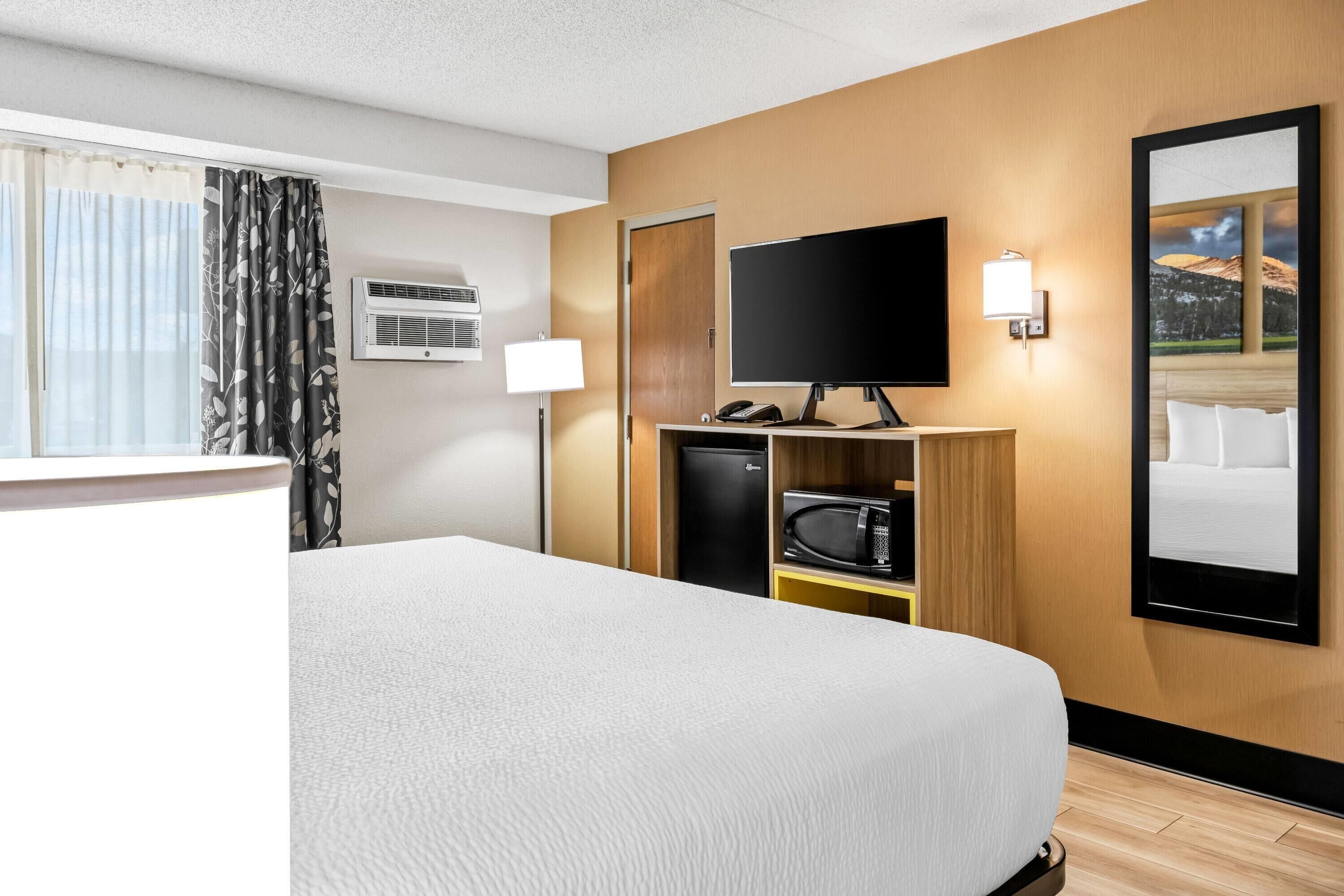 Hotellihuone, jossa on suuri sänky, televisio, työpöytä lampun kanssa, mikroaaltouuni ja jääkaappi.