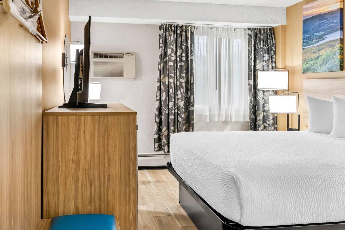Ein Hotelzimmer mit einem Bett, einem Schreibtisch mit Computer, einer Klimaanlage und einem Bild an der Wand.