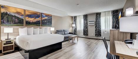 A modern hotel room with a large bed, a desk, a chair, and a sofa.