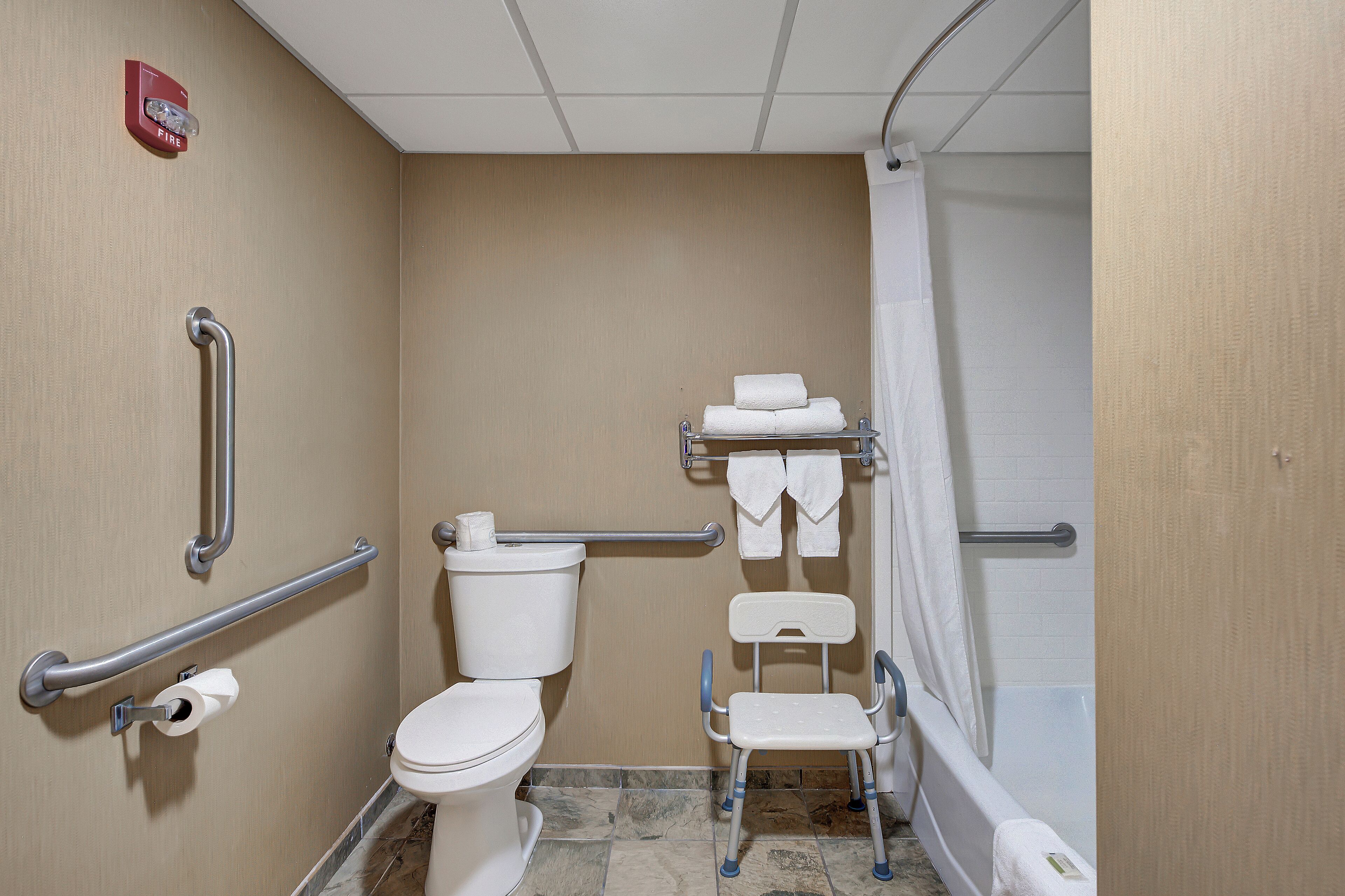 A bathroom with a toilet, grab bars, a shower, and a wheelchair-accessible bench.