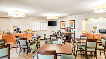 Un comedor de hotel con mesas y sillas de madera, una zona de cocina con televisor y una ventana con vistas.