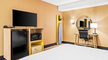Camera d'albergo con un letto, una scrivania con una sedia, una televisione, un forno a microonde, un frigorifero e uno specchio.