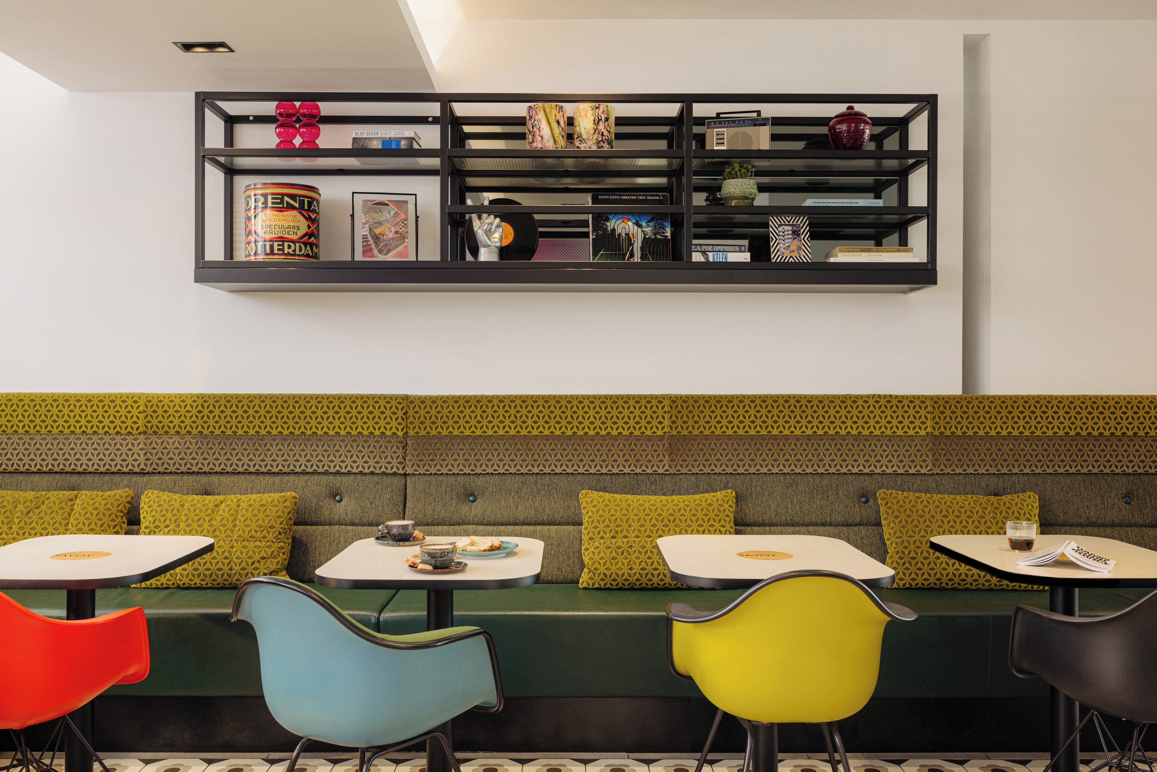 Een modern interieur met een groene, gestreept bankje, kleurrijke stoelen en een zwarte plank met diverse spullen.