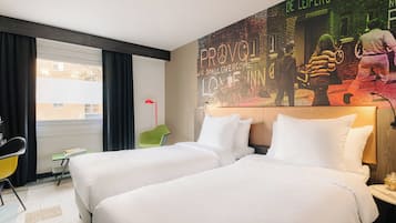 Una habitación de hotel con dos camas, una silla verde, un escritorio y un mural grande en la pared.