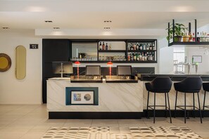 A modern bar area with a marble countertop, black bar stools, and a shelf with bottles and glasses. - Leonardo Hotel Rotterdam Savoy (Rotterdam)