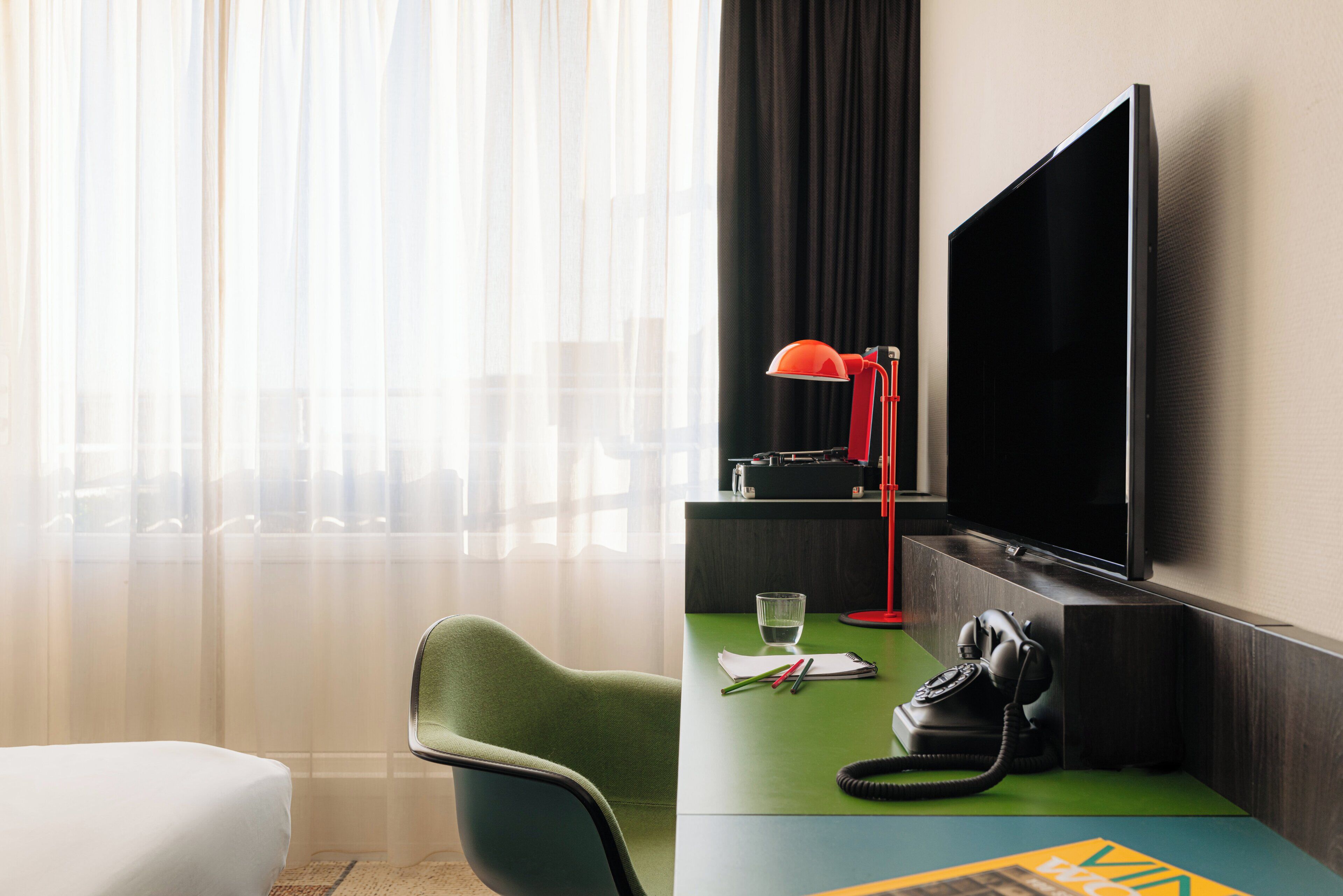 Een hotelkamer met een bed, een bureau met telefoon, een televisie en een stoel.