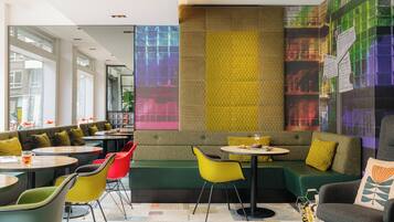 A modern restaurant with green seating, yellow and red chairs, and a patterned wall.