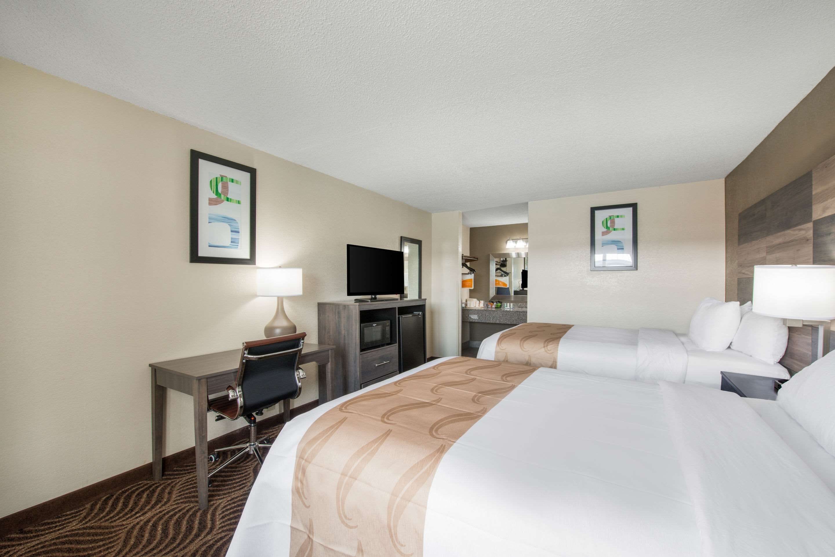 Una habitación de hotel con una cama grande, un escritorio con una silla, un televisor y un espejo.
