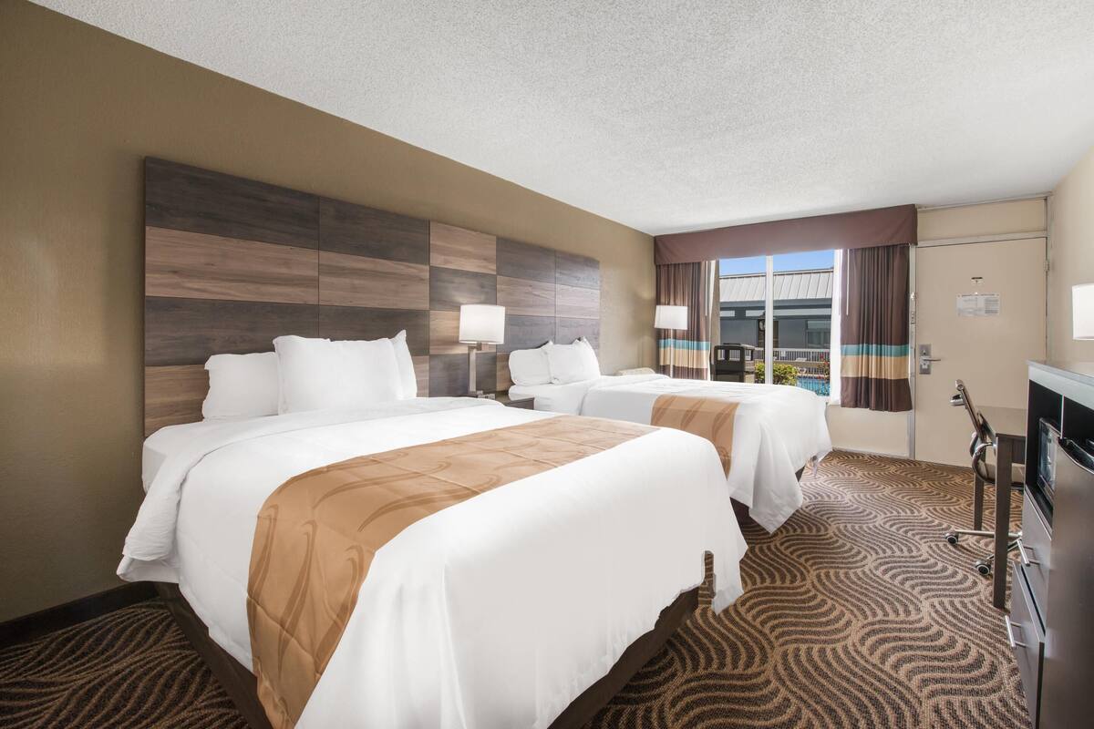 A hotel room with two beds, a large window, a flat-screen TV, and a desk.