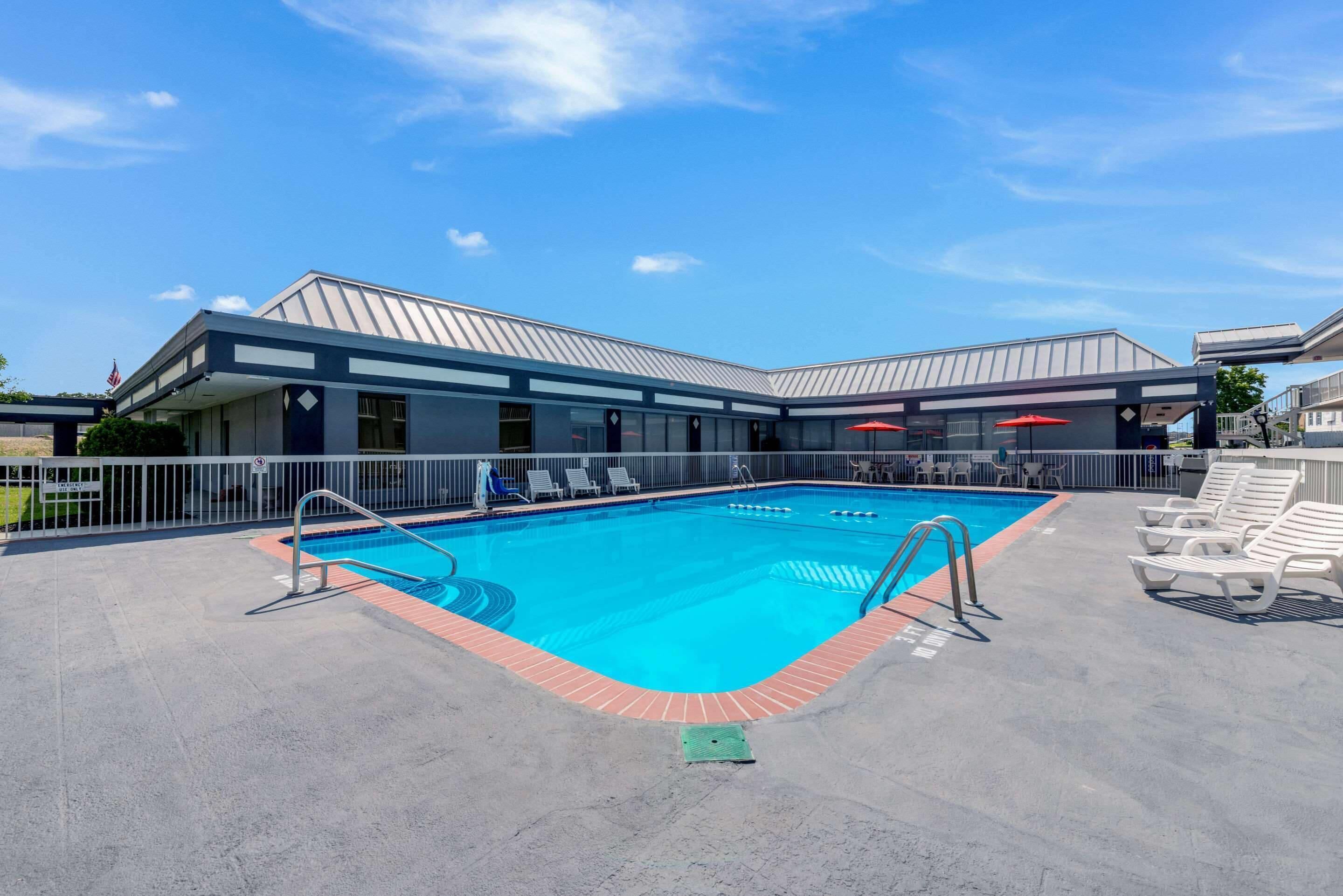 A swimming pool with a metal roof, surrounded by lounge chairs and a covered seating area.