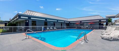 A swimming pool with a metal roof, surrounded by lounge chairs and a covered seating area.