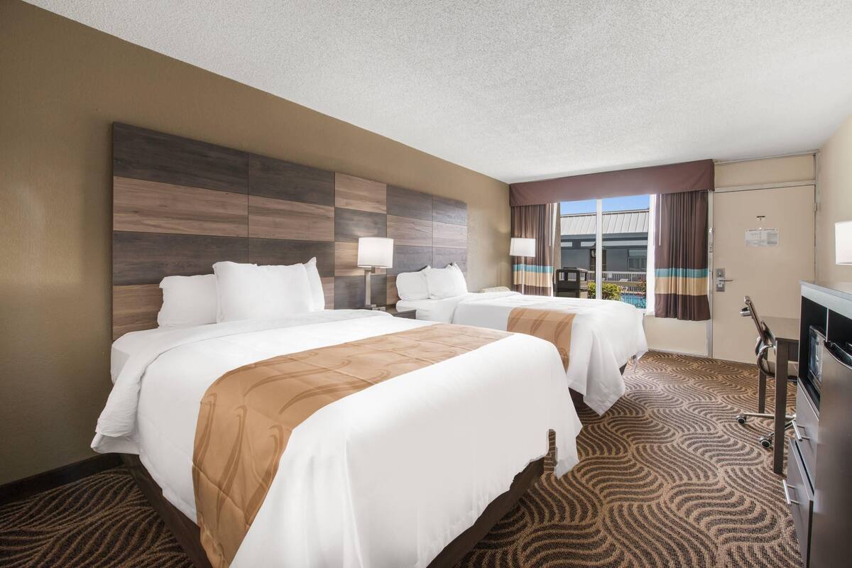 A hotel room with two beds, a large window, a flat-screen TV, and a desk.