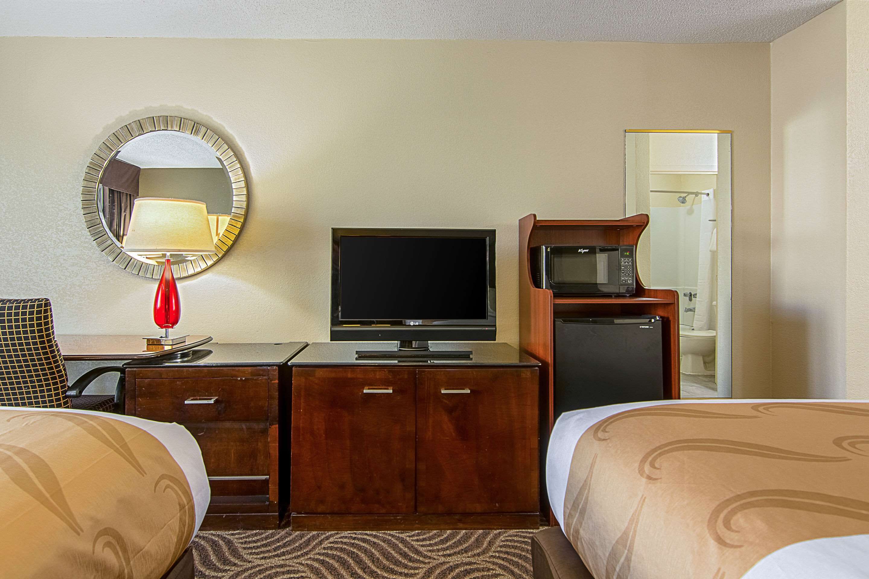 Ein Hotelzimmer mit Fernseher, Mikrowelle, Schreibtisch mit Lampe und zwei Betten.