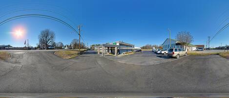 A parking lot with several cars, a building with a green roof, and a clear blue sky.